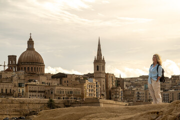 Valletta, Malta A tourist woman stands on a rocky outcrop rocky  with a view over old Valletta and the Valletta Cathedral.