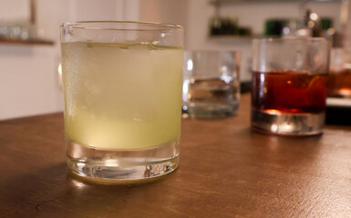 Close-up of assorted cocktails on a wooden bar counter, with a focus on a frosted green cocktail, creating a relaxed, cozy ambiance ideal for bars and lounges.