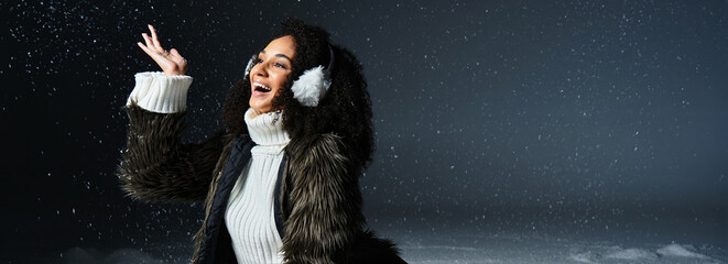 A joyful brunette woman showcases her winter style, wearing earmuffs and a faux fur jacket as she...