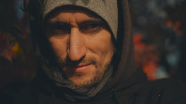 Warm Smile &ndash; Young man in black hoodie and gray hat in autumn forest, close-up, red leaves hanging, warm sunlight on face, smiling mischievously, cozy, joyful, happy 