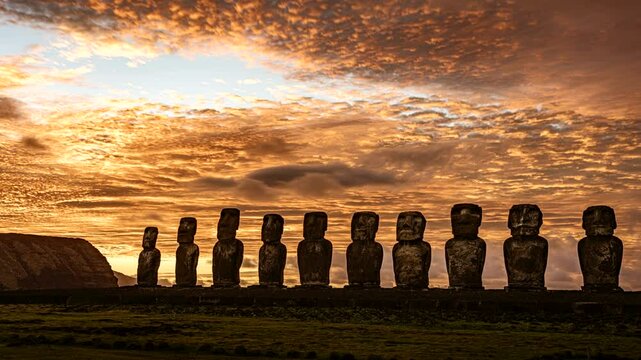 The sun rises behind a row of ancient moai statues on easter island, casting a warm glow on the landscape