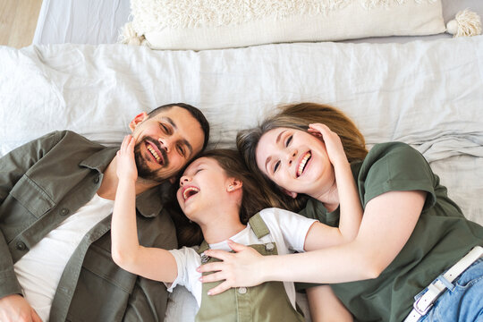 Happy family at home. Mother father children daughter relaxing in bed at home indoor. Mom dad parents kid girl relax playing hugging having fun together. Family smiling laughing enjoying tender moment