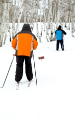 Two people skiing in the snow with orange and blue jackets