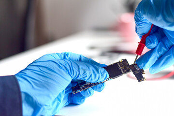 A technician wearing repair gloves is using a meter to measure abnormalities in the electronic...