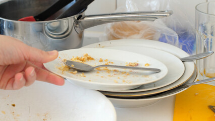 Close up of a human hand putting away a dirty plate on another dirty plate on a very messy kitchen...