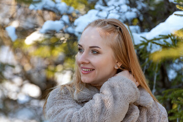 Portrait of young red-haired girl against of snow-covered fir trees and pine trees. Girl in winter snowy scenery, park or forest.