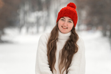 Portrait of cute girl on winter forest background. Smiling young woman with long hair in red hat...