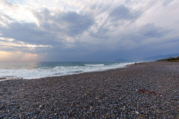 Serene Pebble Beach at Sunset with Radiant Sky and Ocean Waves..