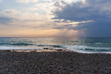 Serene Pebble Beach at Sunset with Radiant Sky and Ocean Waves..