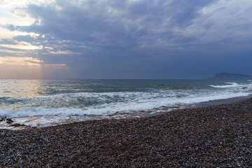 Serene Pebble Beach at Sunset with Radiant Sky and Ocean Waves..