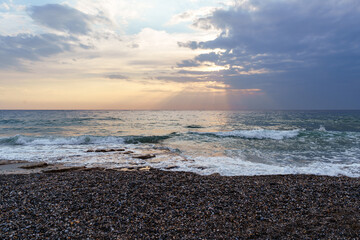Serene Pebble Beach at Sunset with Radiant Sky and Ocean Waves..