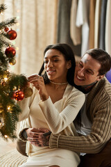 Together they hang ornaments on their beautifully lit Christmas tree, sharing laughter.