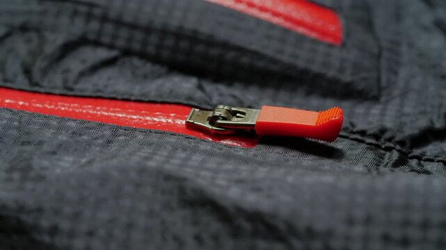 Macro footage showcases a close-up of a zipper slider opening and closing a red waterproof zipper on a gray jacket, highlighting intricate details of the textile and fastener
