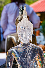 Transparent glass buddha statue in meditation posture among various buddha statues on the blurry...