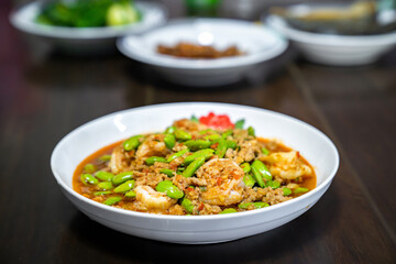 Thai Stir-Fried Stink Beans with Shrimps and spicy shrimp paste sauce in white dish bowl on dark wood table.