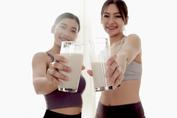Two glasses of milk in hand of sporty girl buddy. Happy beautiful Asian women hold milk glass for drinking after workout exercise. Food rich in vitamins and calcium. Healthy food and sport lifestyle