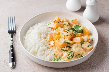 Bowl of pumpkin in sour cream sauce with rice sprinkled with fresh parsley on beige textured stone table, top view. Vegetarian food