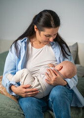 Fototapeta premium Mother breastfeeds her cute newborn baby sitting on her bed at home. Milk from mother breast is a natural food and medicine for babies.