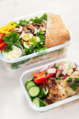 Lunch box containers with grilled chicken breast and fresh vegetable salad.