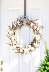 An elegant beach-themed wreath adorned with seashells and starfish perfectly complements a white front door. Ideal for coastal homes, this decor adds a touch of marine elegance and serenity.

