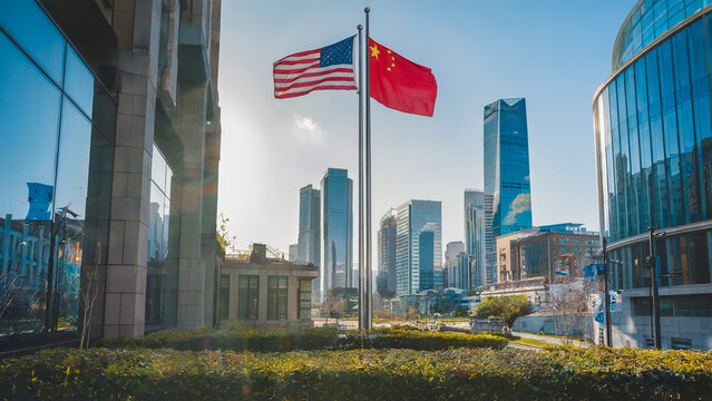 The U.S. and China flags flying together in a lively urban setting, with a modern skyline and skyscrapers gleaming in the sunlight. - Powered by Adobe
