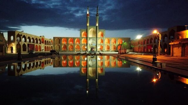 Amir chakhmak mosque in yazd glows beautifully at dusk, its reflection shimmering in the water, under a dramatic evening sky