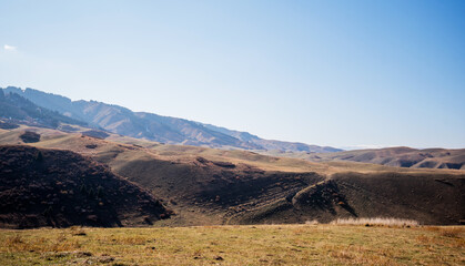a vast, rolling hills landscape with a clear, expansive sky. The earthy tones of the hills on the end of autumn or early winter, with sparse vegetation and the distant mountains showing of snow
