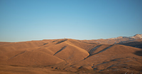 Golden hour light casting long shadows over undulating hills and dry grassland in a serene, high-altitude mountain landscape.