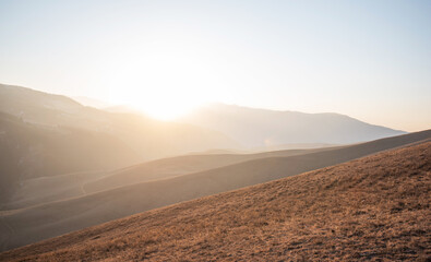 Fototapeta premium Soft sunrise light washes over a peaceful highland meadow with gentle rolling hills and the silhouette of mountains in the background