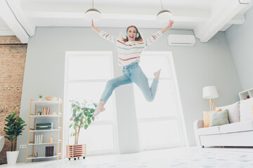 Fototapeta premium Young woman enjoying leisure time jumping with joy in modern living room