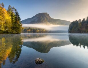 Fototapeta premium Peaceful Lake at Sunrise, With Mist Rising From the Water and a Lone Mountain Reflecting on the Calm Surface, Surrounded by Autumn Forests in Soft Morning Light