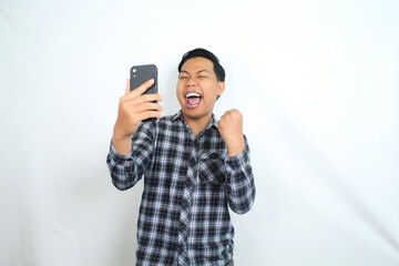 successful asian man raising fist with holding smartphone wearing casual shirt isolated on white