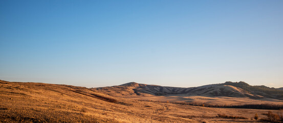 Expansive golden grassland with rolling hills under a clear sky at sunset, conveying a sense of vast open space and tranquility