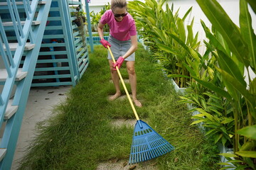 A woman raking the lawn at the backyard of her house 