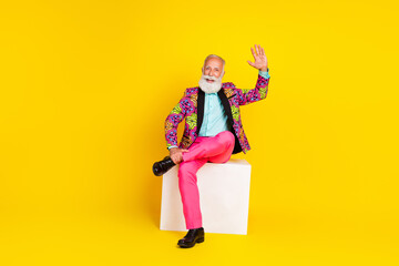 Full body photo of senior male sit white platform wave hand hi wear trendy colorful pink fancy outfit isolated on yellow color background