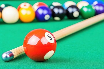 A red billiard ball with the number 9 on it sits on a green felt pool table with a cue stick in front of it, other balls are blurred in the background.