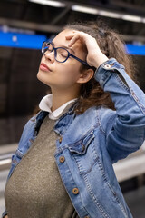 Pretty young girl with glasses and closed eyes poses with hand on head