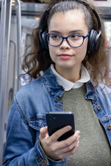 Pretty young girl listening to music with headphones and looks at her phone inside the train