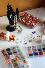 Hand figurine, colorful friendship bracelets, necklaces, various beads and DIY supplies on the table. Making jewelry at home. Selective focus.