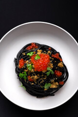 Black pasta with cuttlefish ink and red caviar, served with breadcrumbs fried in olive oil. Volcanic inspiration, seafood paste, black background, minimalist composition. Modern pasta with seafood
