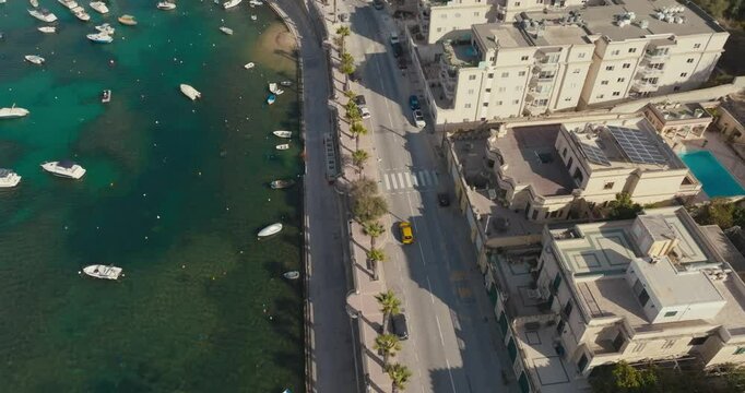 Aerial view of Bugibba on the island of Malta. Urban landscape of a city on the seashore with streets and roads with boats and yachts in the marina. High quality 4k footage