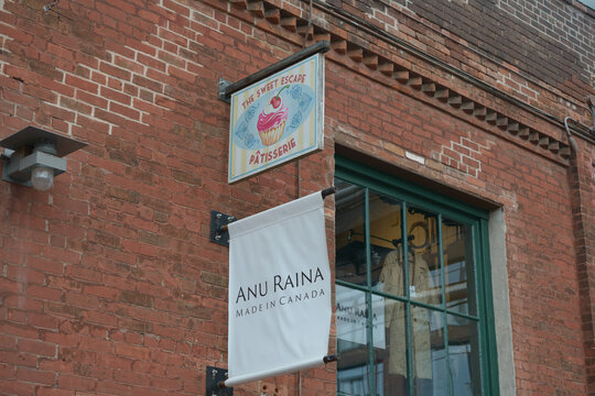 The Sweet Escape and Anu Raina signs projecting from a historic building at 24 Tank House Lane, Distillery District, Toronto, Canada