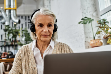 A mature woman with gray hair listens attentively during her virtual gathering in a warm atmosphere.