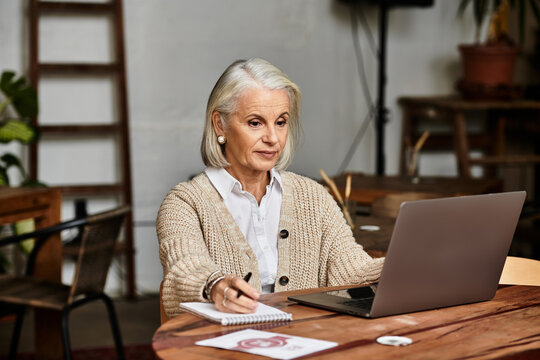 A beautiful woman with gray hair works intently on her laptop while enjoying a drink. - Powered by Adobe