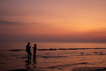 Fototapeta premium a sunset with people standing in the water and one is wearing a pink and orange sunset