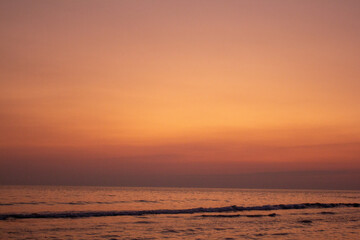 a sunset with people standing in the water and one is wearing a pink and orange sunset