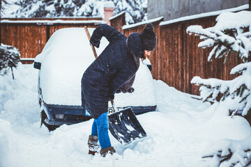 woman with shovel cleaning snow aeound car. Winter shoveling. Removing snow after blizzard © Melinda Nagy