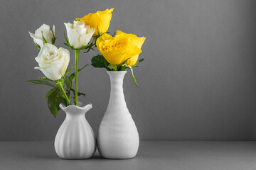 Two small ceramic vases with white and yellow roses on a gray background with a place for copying.