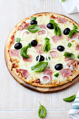 Pizza with ham, green pepper, mozzarella cheese and black olives. Wooden background. 