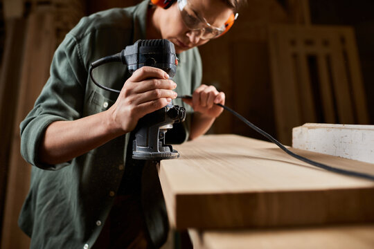 A dedicated carpenter is focused on shaping wood using a power tool in her workshop, showcasing her craftsmanship.